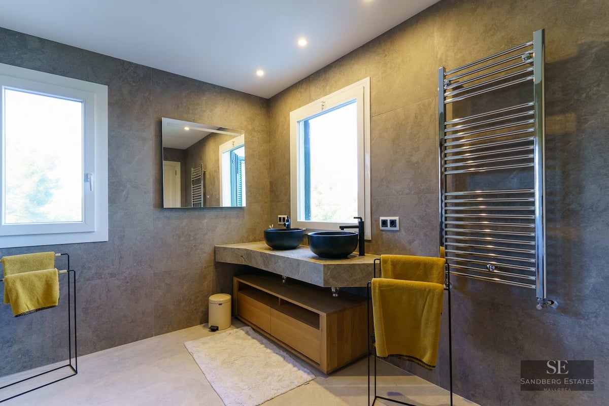Contemporary bathroom with grey stone walls, double black bowl sinks on a floating stone vanity, and a large towel warmer.