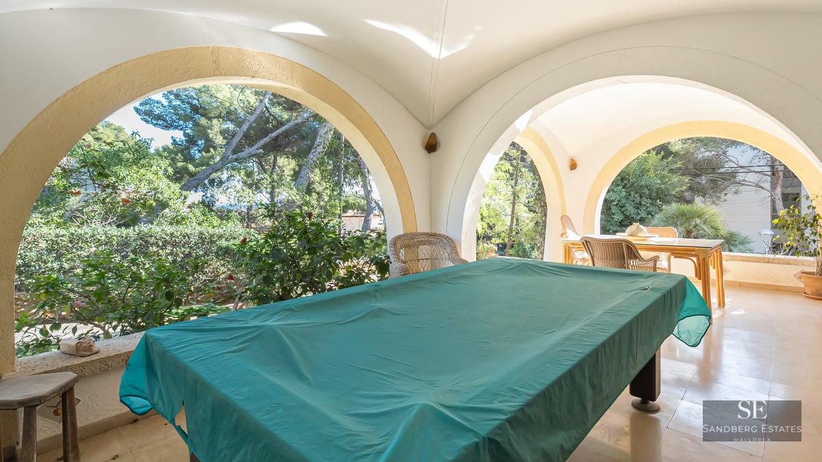 Large covered terrace with white arches, a pool table covered in green cloth, and garden views.