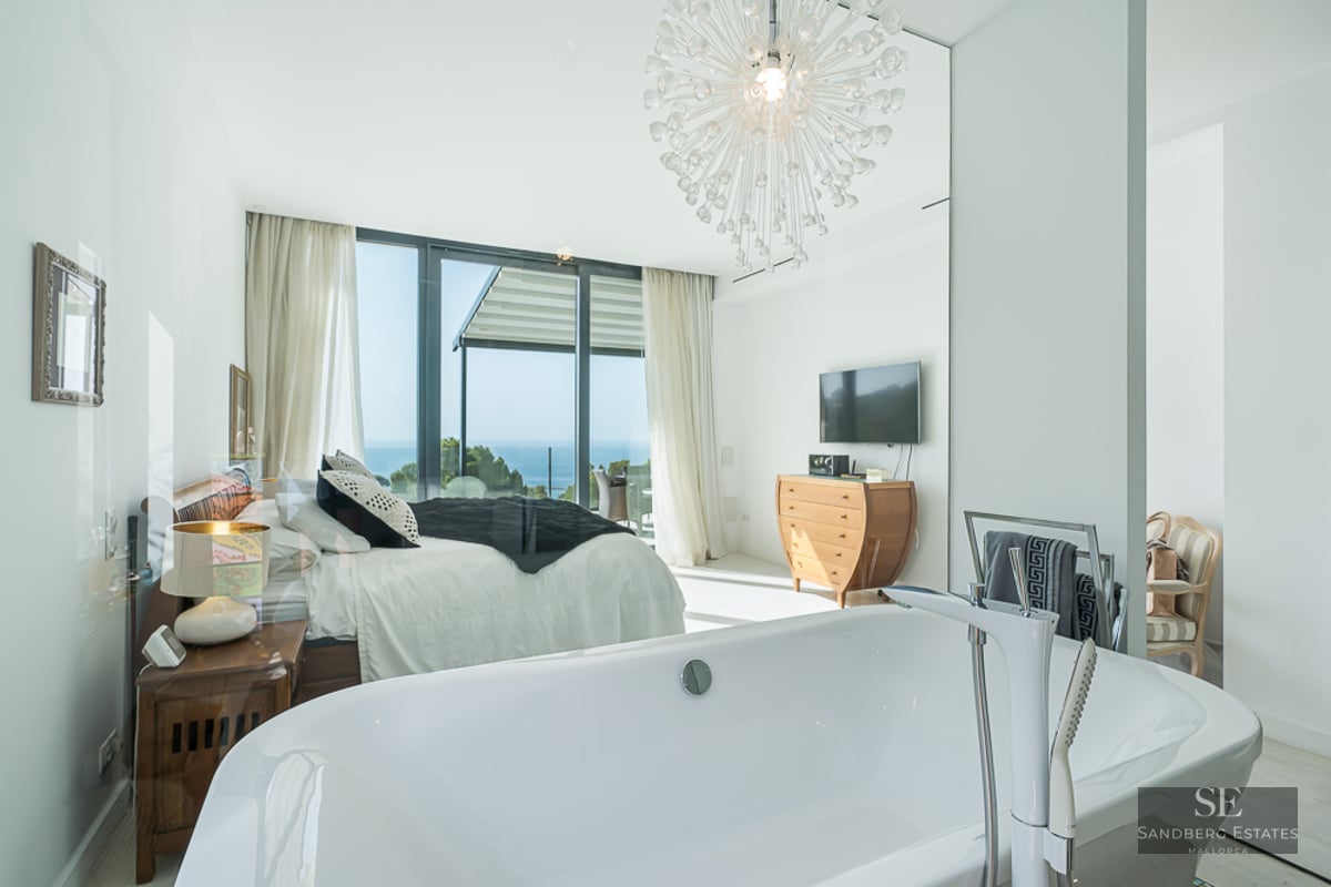 Modern master suite featuring a white freestanding bathtub in the foreground and a large bed with a sea view.