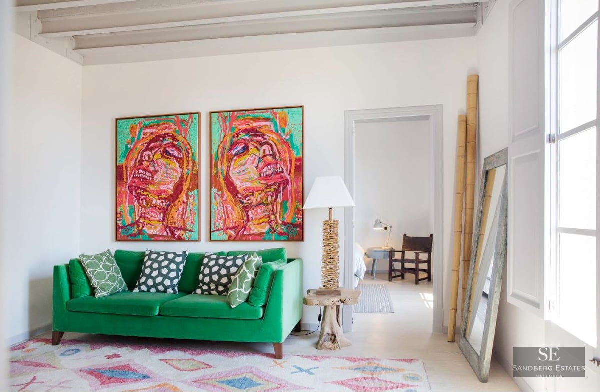 Bright living room featuring a green velvet sofa, two large colorful portraits, and high beamed ceilings.