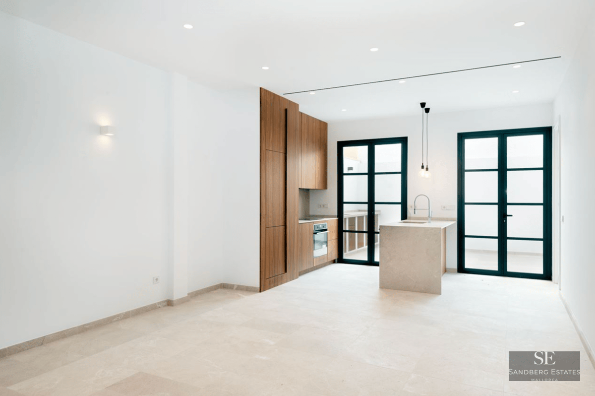 Modern kitchen with wood cabinets, stone island, and large black-framed glass doors leading to a terrace.