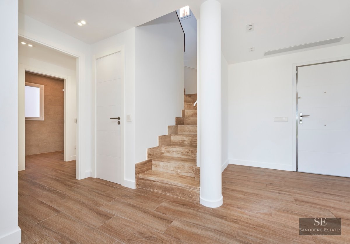 Modern hallway featuring a light stone staircase, white walls, wood-look porcelain floors, and a white structural column.
