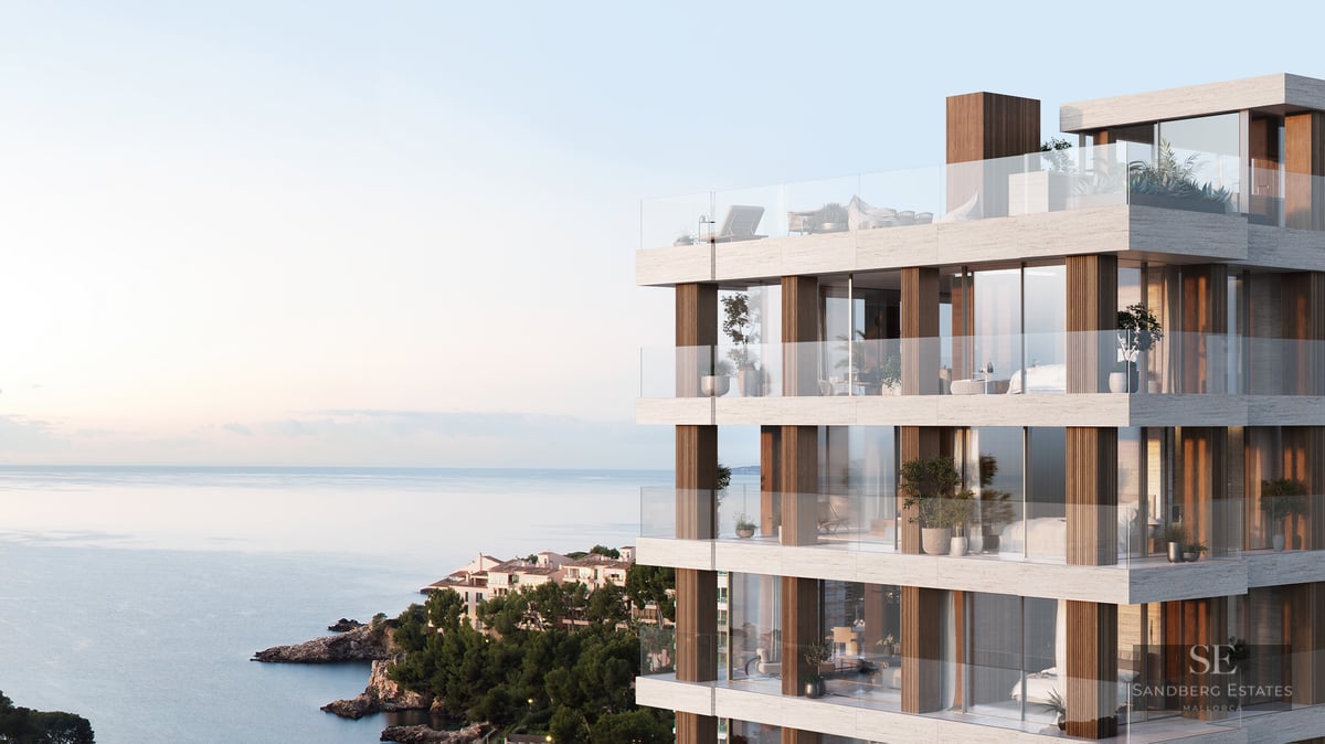 Modern multi-story building with stone facade, glass balconies, and panoramic sea views at sunset.