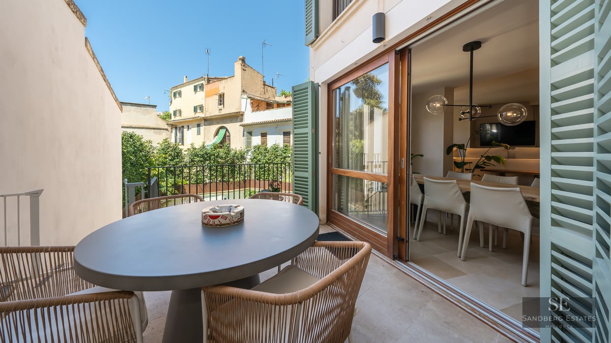 Sunny terrace with a gray oval dining table and wicker chairs next to large sliding glass doors.