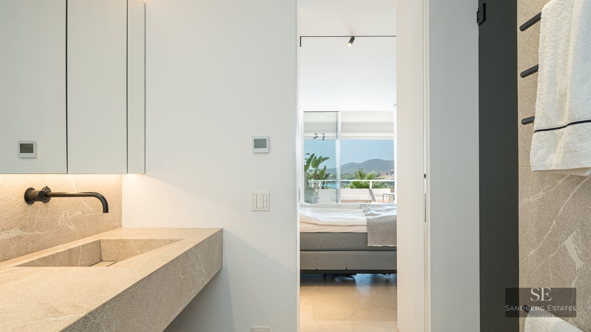 Modern bathroom with a stone sink and black faucet, looking through a doorway into a bedroom with a mountain view.