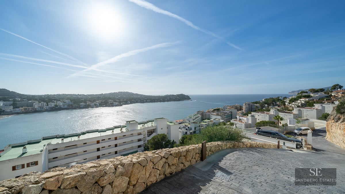 Elevated view of a blue Mediterranean bay with white coastal buildings under a bright sunny sky.