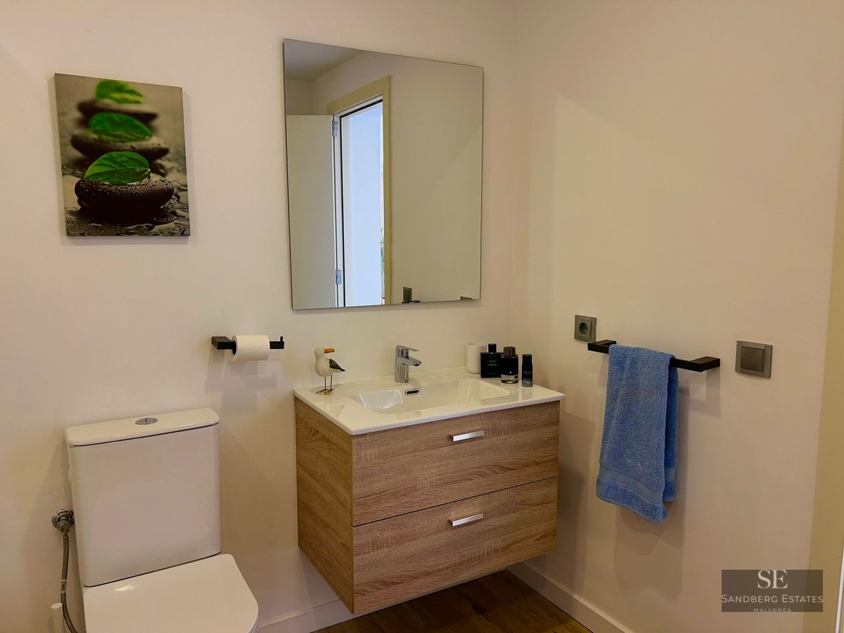 A modern bathroom featuring a floating wood vanity, white toilet, and minimalist decor.