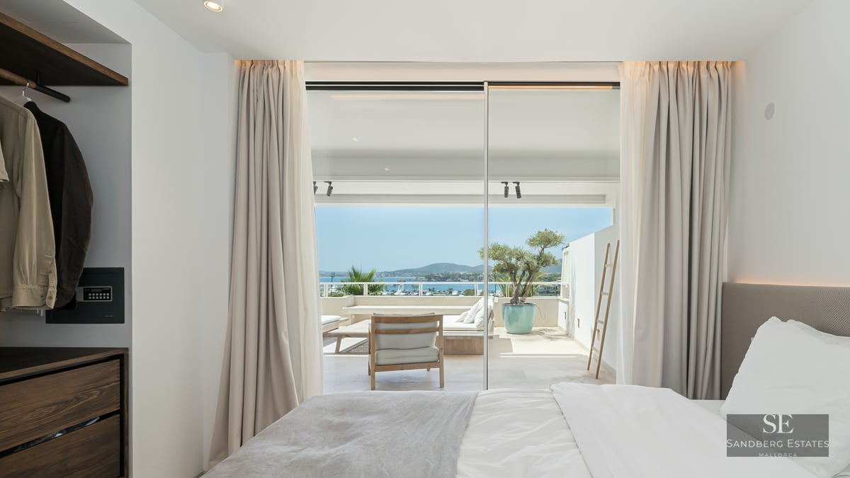 Bright master bedroom featuring floor-to-ceiling glass doors opening onto a sunny terrace with Mediterranean sea views.
