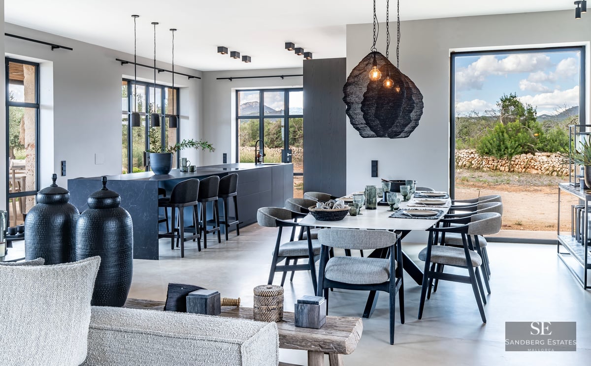 Elegant dining area featuring a long table, dark kitchen island, and large windows with countryside views.