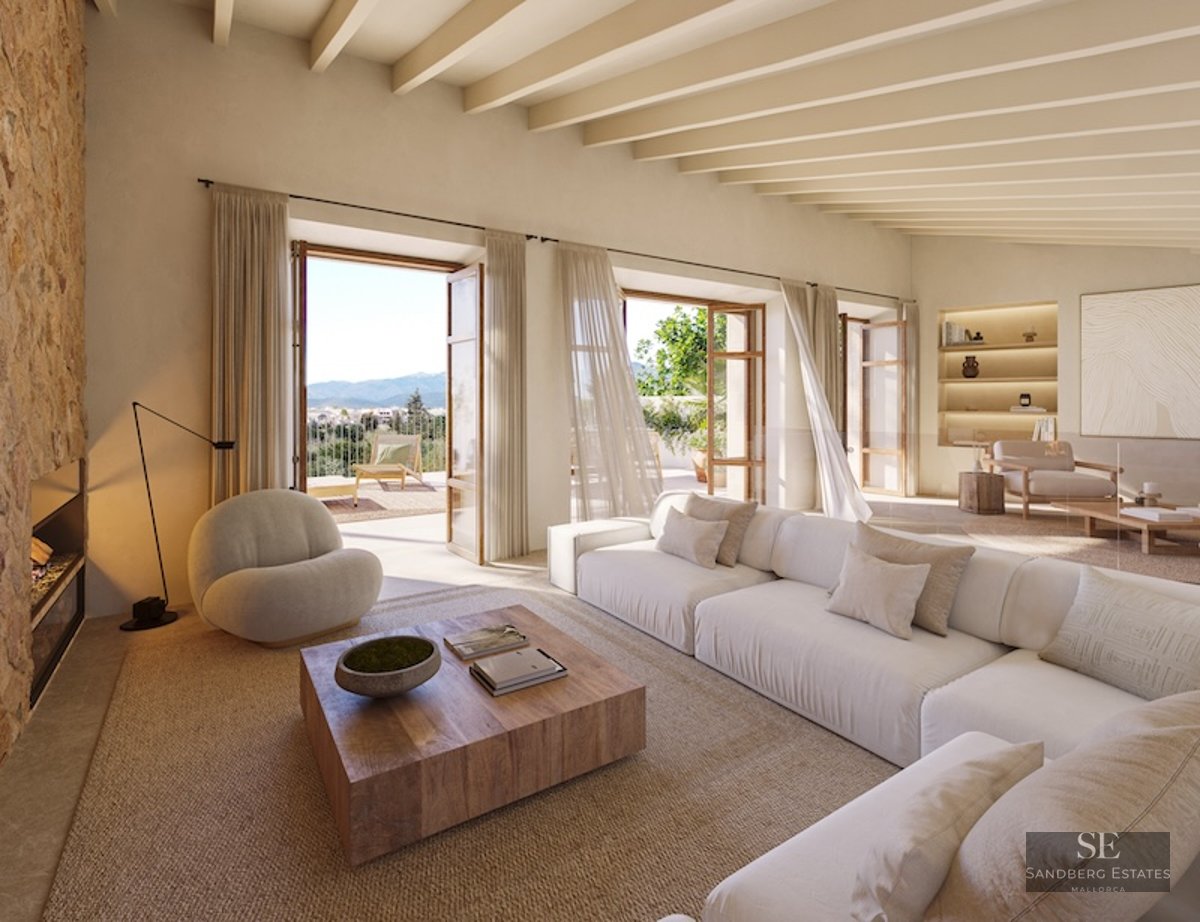 Spacious living room with white sofas, stone wall, ceiling beams, and open doors to a terrace with mountain views.