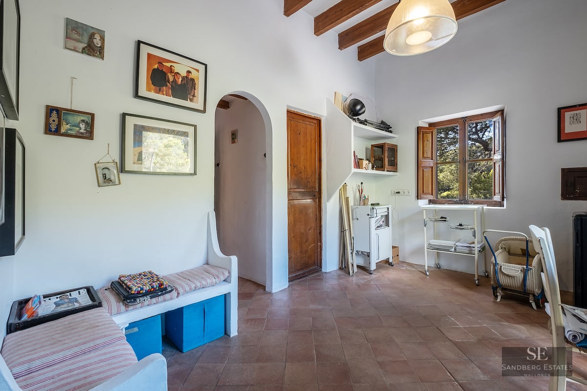 Interior room featuring terracotta floor tiles, exposed wooden ceiling beams, white walls, and a built-in bench.