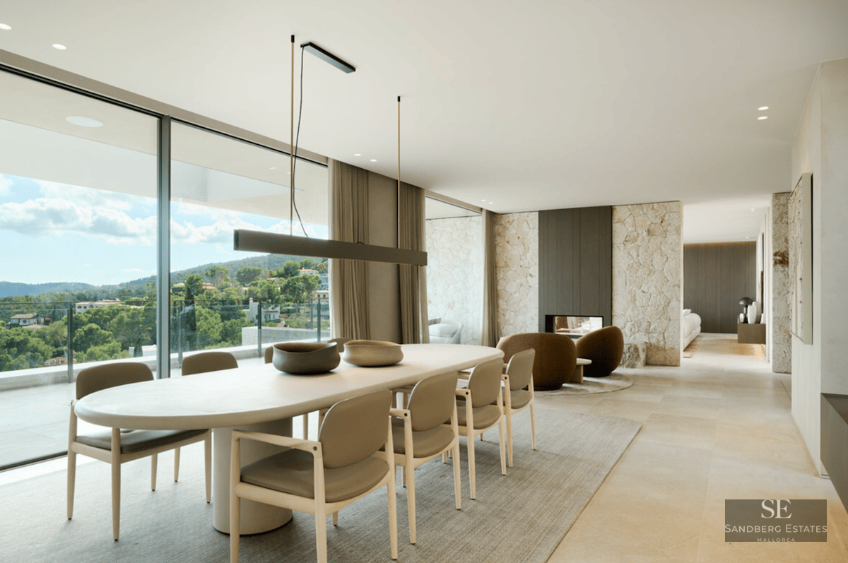 Modern dining area featuring an oval table, stone feature walls, and floor-to-ceiling windows overlooking a lush landscape.