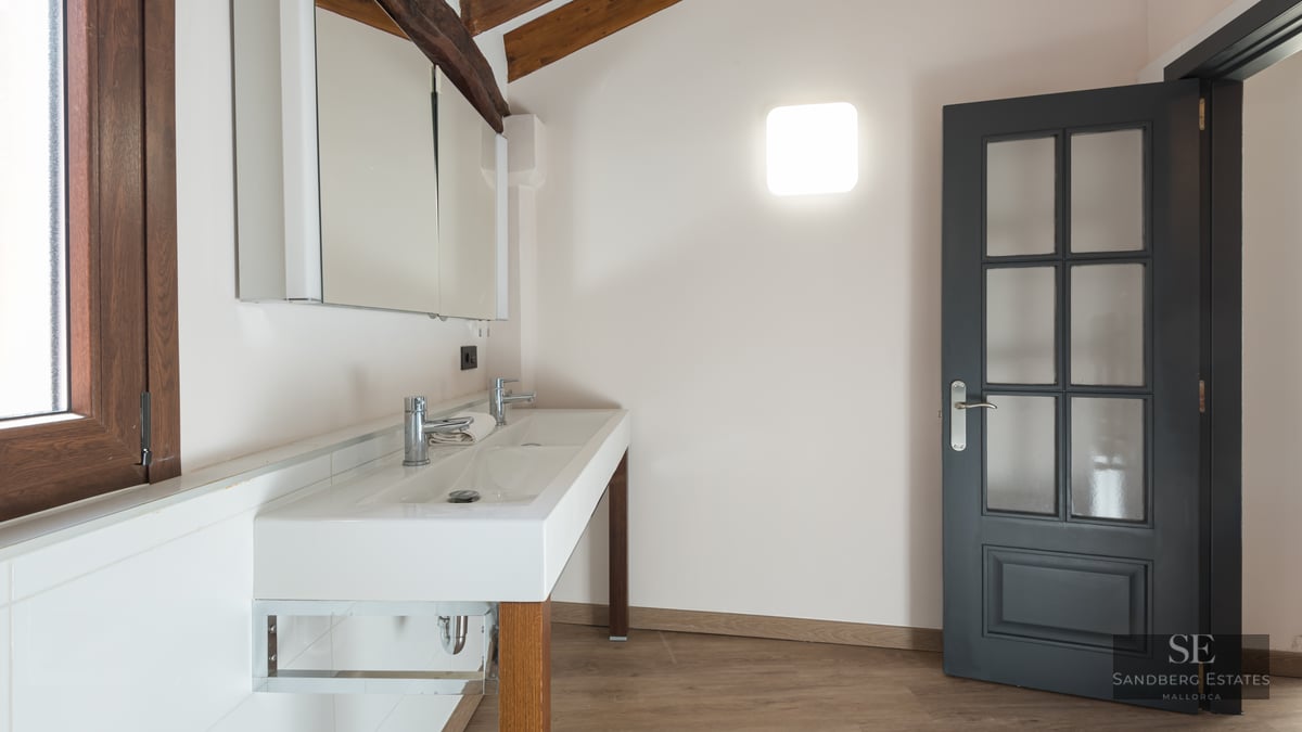 Bathroom featuring a white double sink vanity, exposed wooden ceiling beams, a dark grey door, and a mirror cabinet.