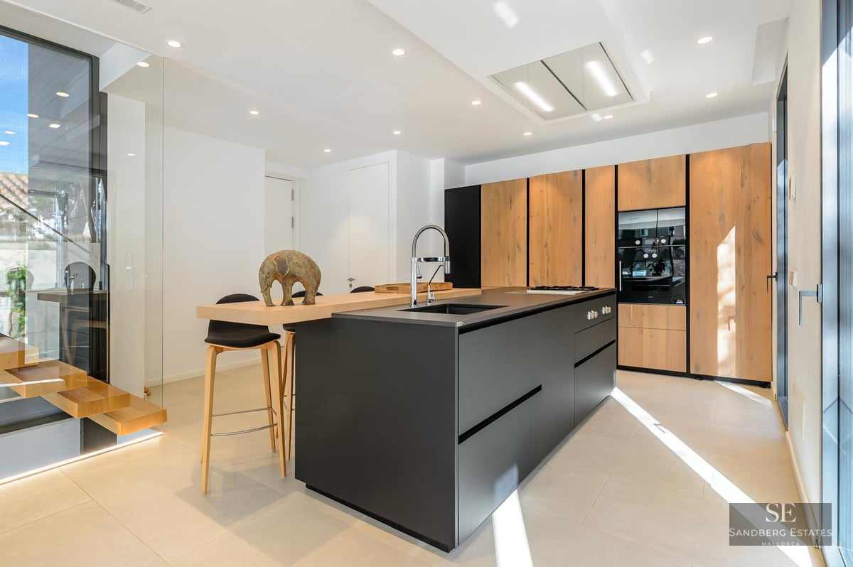 Modern kitchen with a large black island, wood cabinets, and integrated appliances under bright lighting.