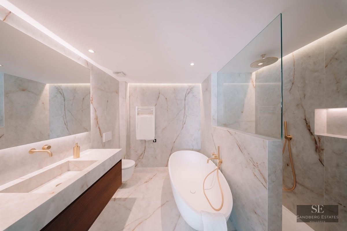 Modern marble bathroom featuring a white freestanding tub, gold fixtures, and an integrated double vanity.