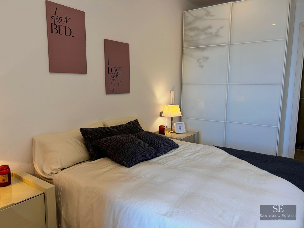 Bedroom featuring a large bed, grey textured pillows, pink wall art, and a large white sliding-door wardrobe.