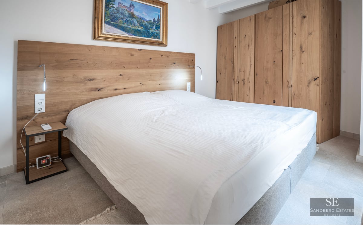 Chambre moderne avec grand lit, tête de lit et armoire en bois clair et un tableau classique.
