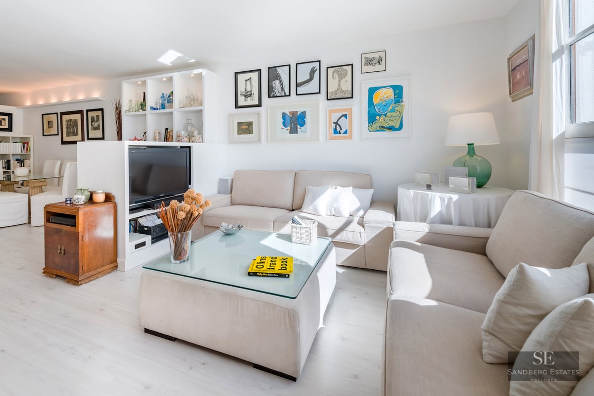 Spacious living room featuring beige sofas, a glass-topped ottoman coffee table, and an extensive art gallery wall.