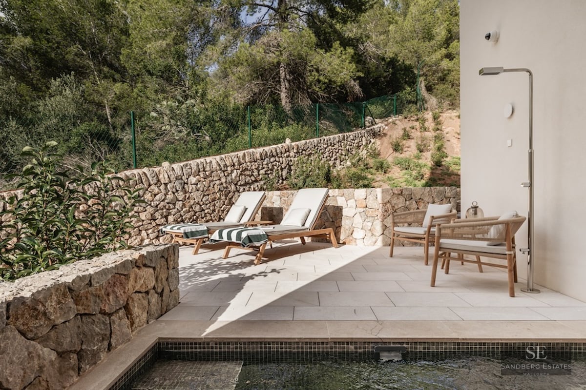 Modern stone terrace featuring designer sun loungers, a metallic outdoor shower, and views of a lush forest.