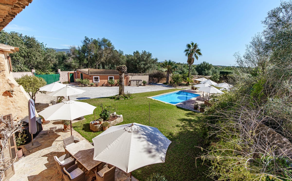Rectangular swimming pool surrounded by green lawn, sun umbrellas, and a stone terrace at a Mediterranean estate.