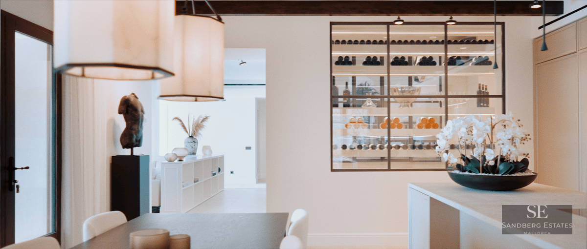 Modern dining area featuring a glass-enclosed wine display, wooden beams, and designer pendant lights.