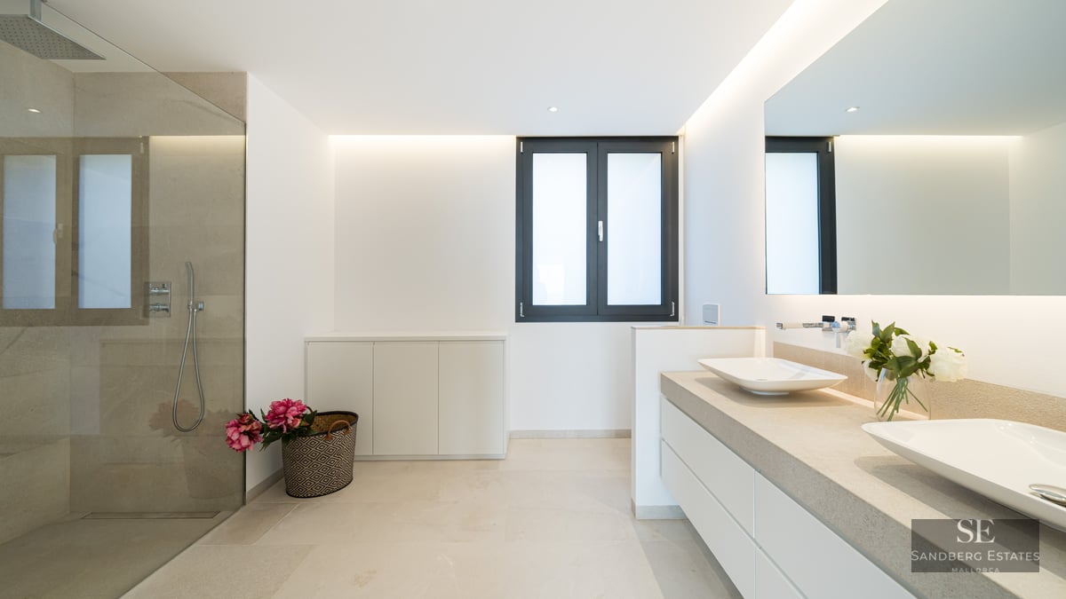 Modern master bathroom with a walk-in glass shower, double vessel sinks on stone counters, and a large backlit mirror.