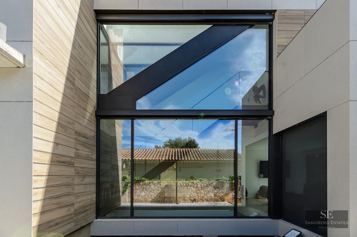 Minimalist facade featuring large glass windows, black frames, and stone and wood cladding.