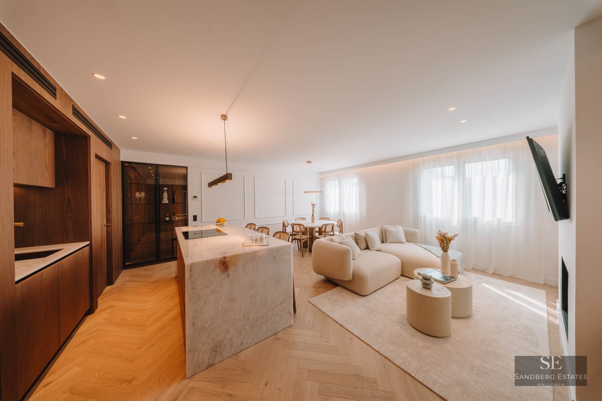 Modern open-plan living room with marble kitchen island, beige sectional sofa, and light wood herringbone floors.