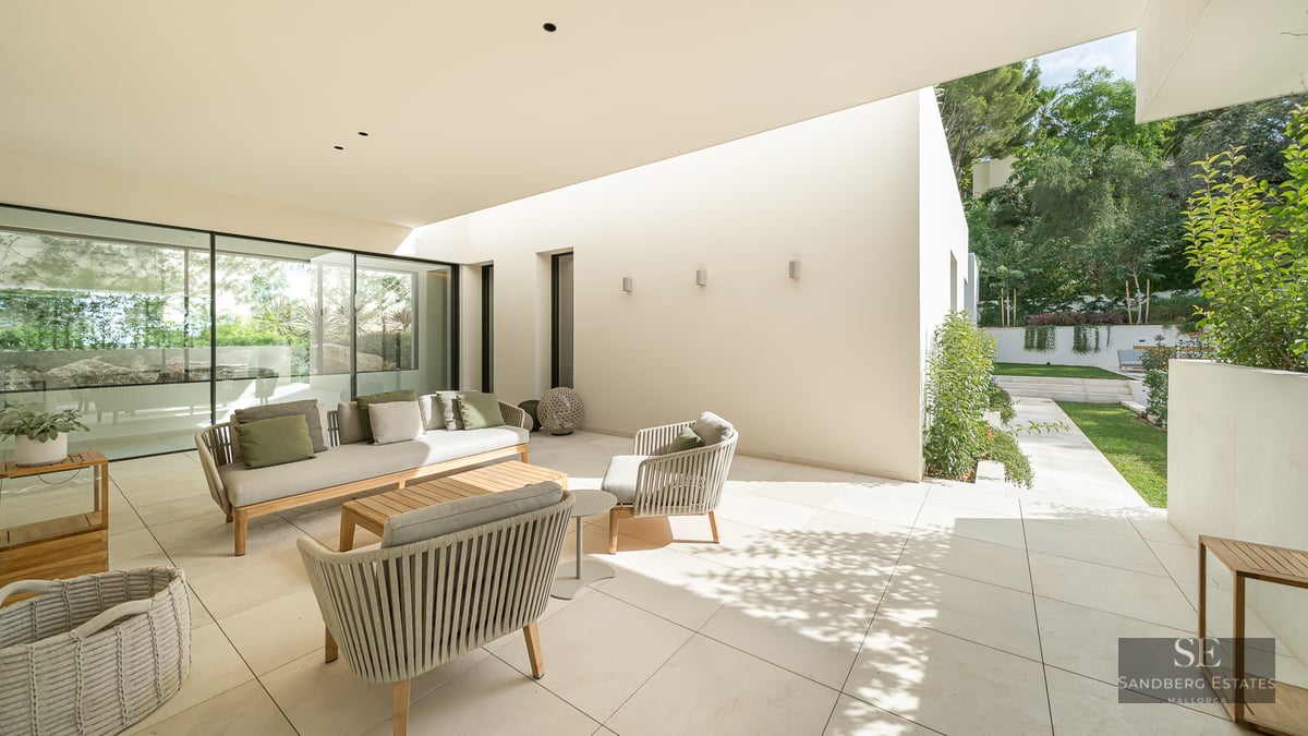 Luxury outdoor terrace with a beige sofa, green cushions, and woven chairs on a stone patio overlooking a garden.