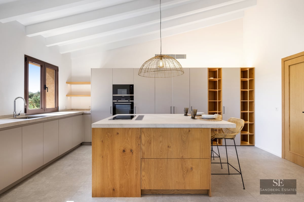 Bright kitchen featuring a large oak island, white beamed ceiling, and integrated lighting in open shelving.