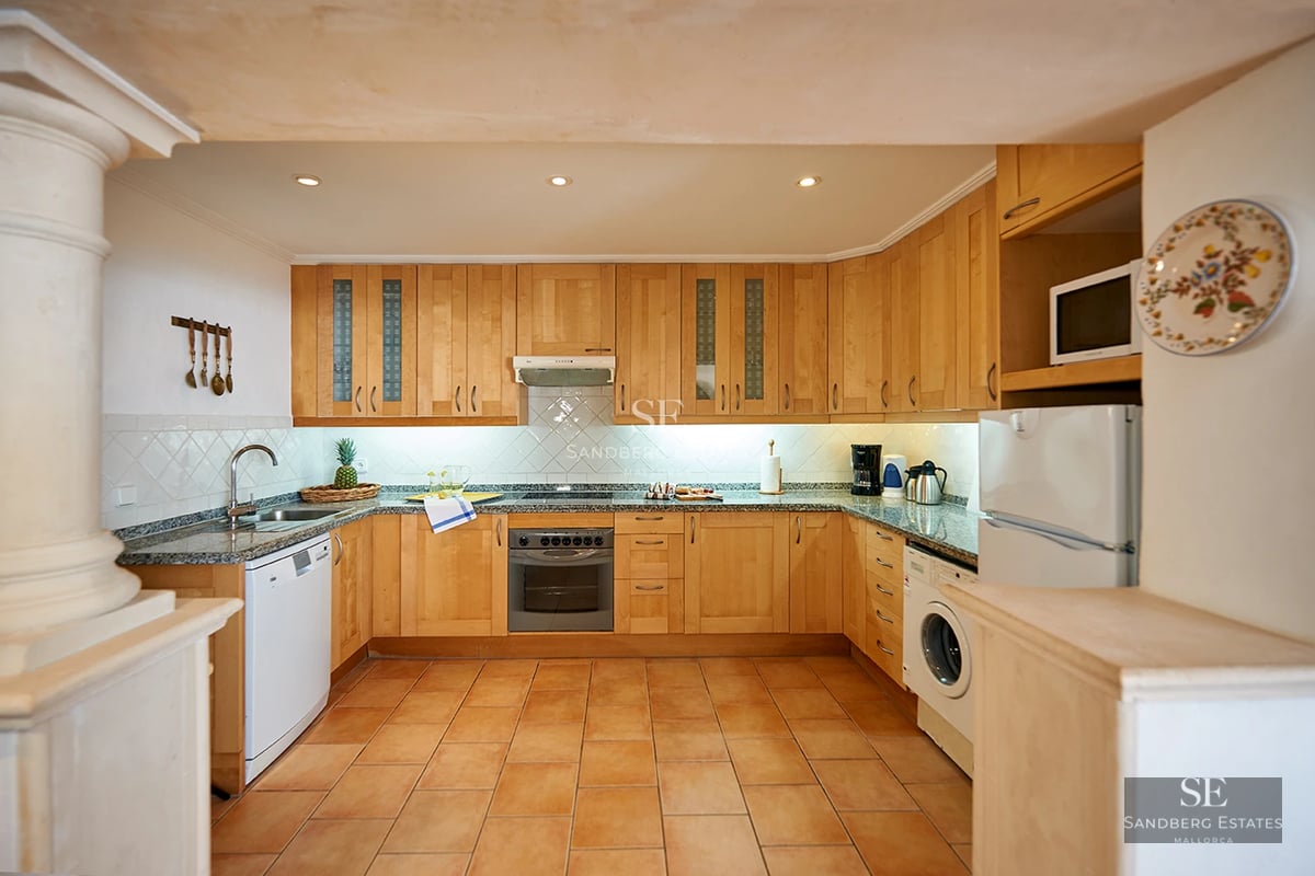 View of an elegant pool with sun loungers and umbrellas, surrounded by lush greenery and a modern house.