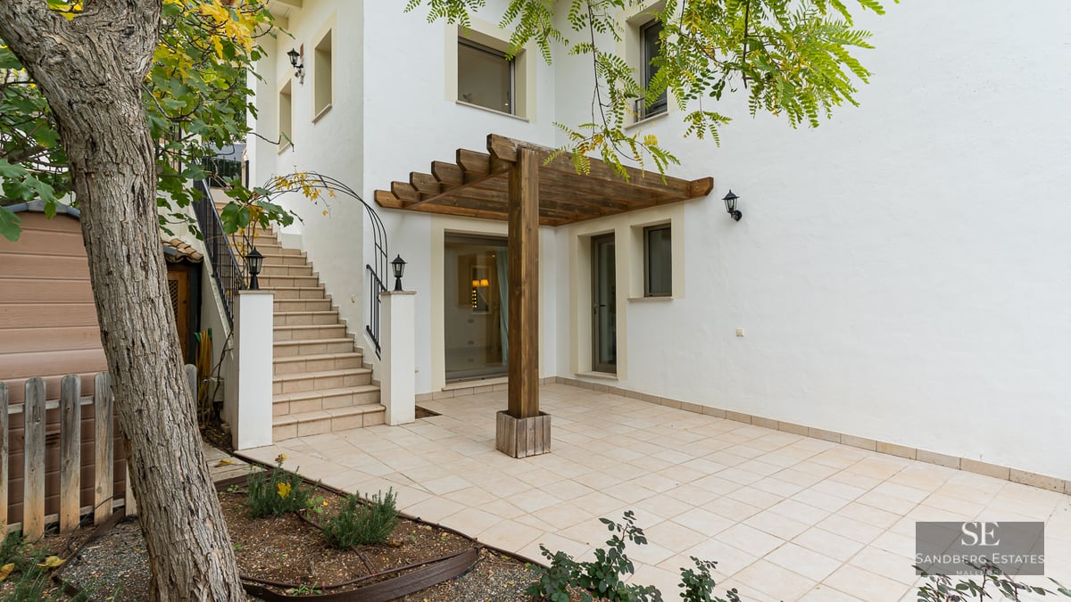 White building exterior with a tiled patio, wooden pergola, and stone stairs leading to an upper level.