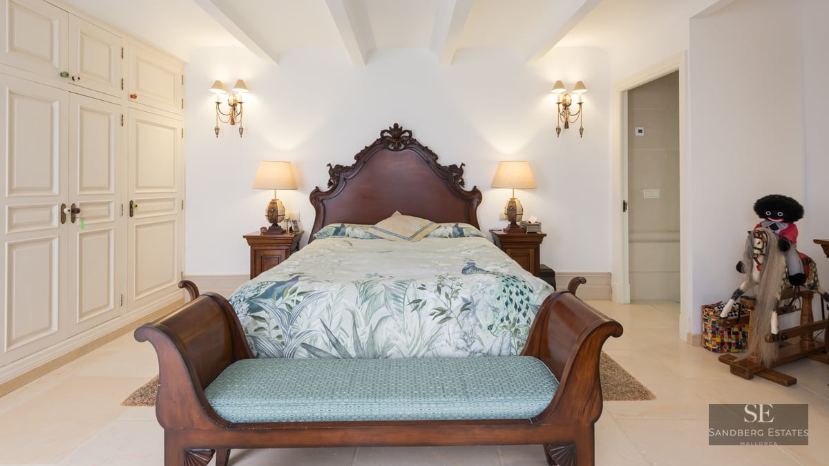 Bedroom featuring a large carved wood headboard, floral bedding, matching nightstands, and built-in white wardrobes.