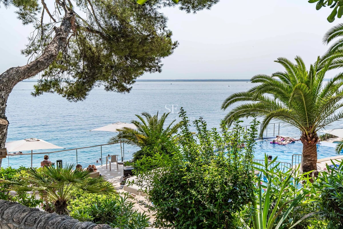 Exterior view of a modern villa featuring an infinity pool, large windows, and minimalist design. Lush greenery surrounds the property.