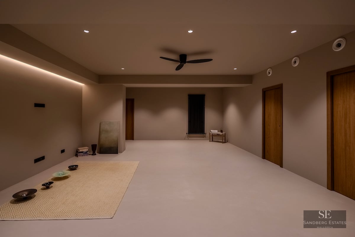 Une grande pièce minimaliste avec un éclairage chaleureux, des murs taupe, des portes en bois et un ventilateur noir.