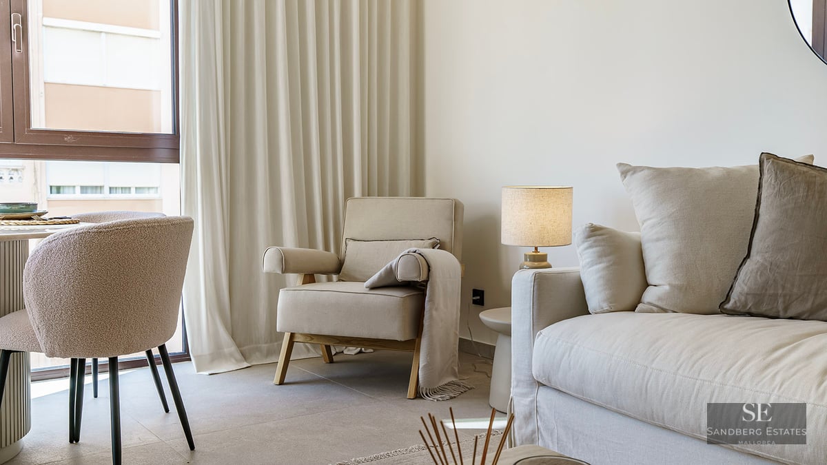 Bright living room corner featuring a cream sofa, armchair, bouclé chair, and soft floor-to-ceiling drapes.