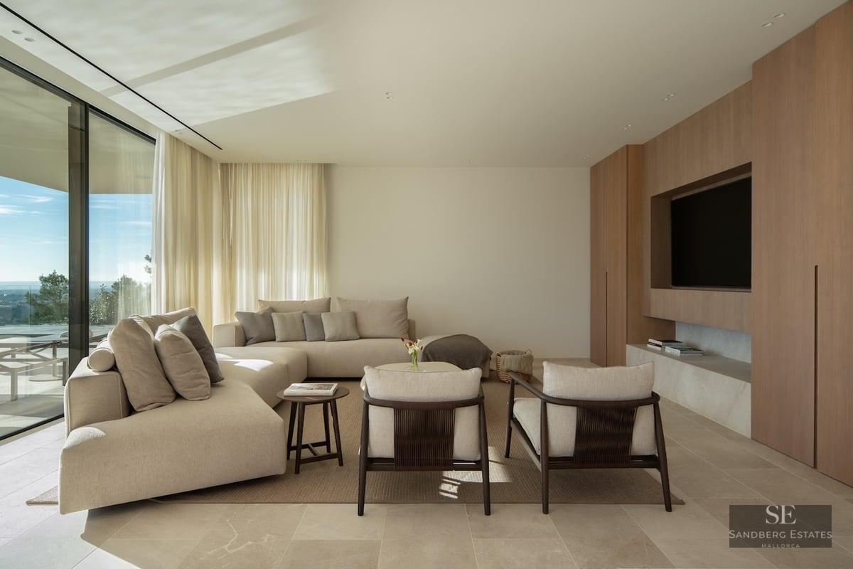 Modern living room with a beige sectional sofa, wood paneled TV wall, and floor-to-ceiling windows with a scenic view.