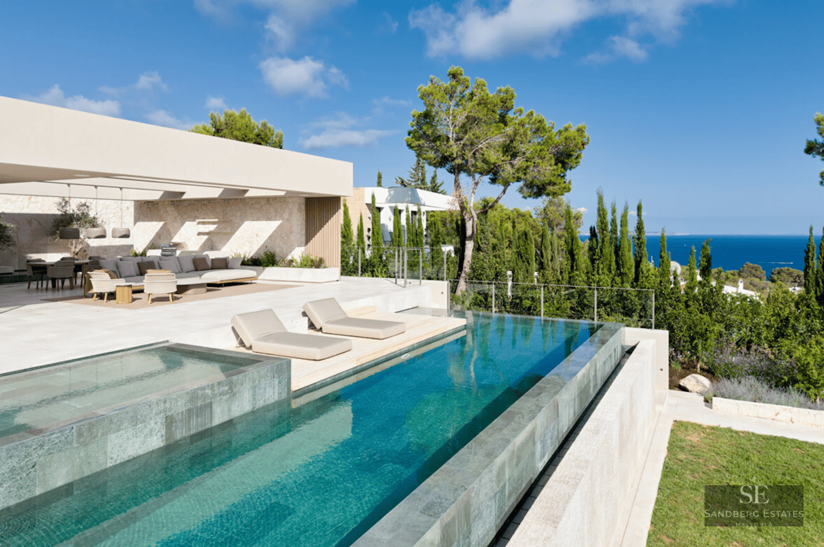 Modern infinity pool with sun loungers overlooking the sea, adjacent to a stylish outdoor lounge and dining area.