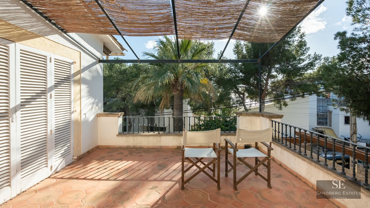 Sunny terrace featuring terracotta tile floor, director chairs, iron railing, and a reed pergola for shade.