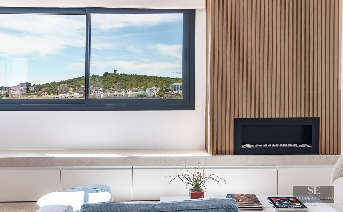Modern living room with slatted wood wall, built-in fireplace, and a large window overlooking a hilltop castle.