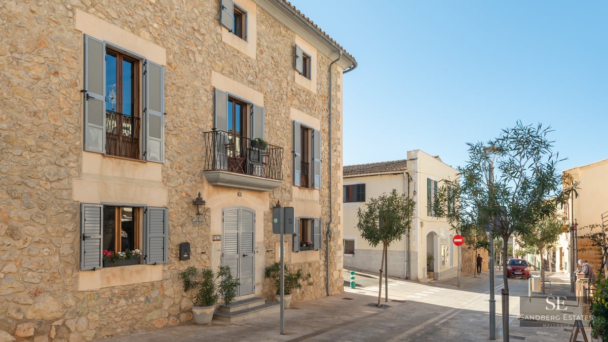 Traditional stone building with grey shutters and iron balconies on a sunny street.