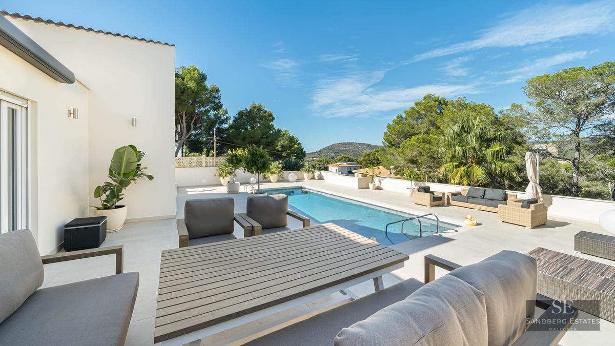 Grande terrasse ensoleillée avec une piscine rectangulaire, mobilier de salon élégant et cadre verdoyant.