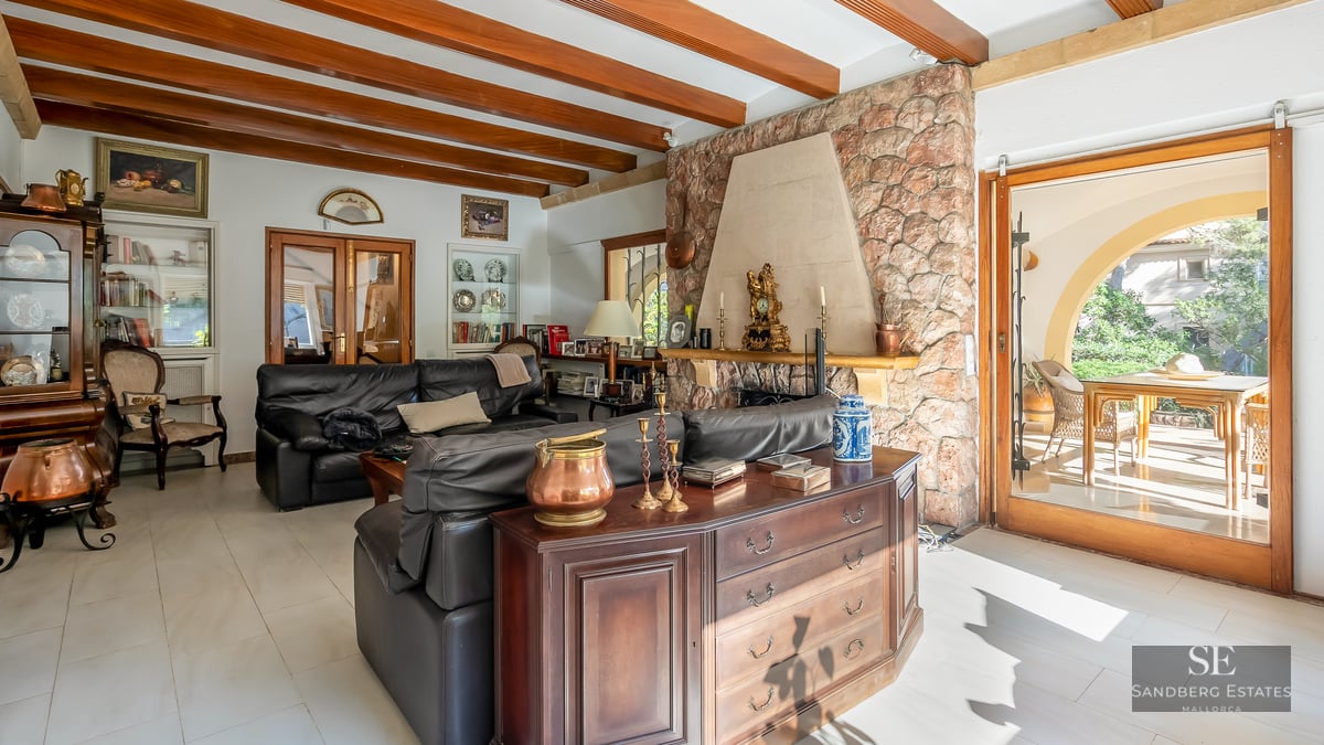 Cozy living room featuring exposed wood ceiling beams, a large stone fireplace, black leather sofas, and terrace access.