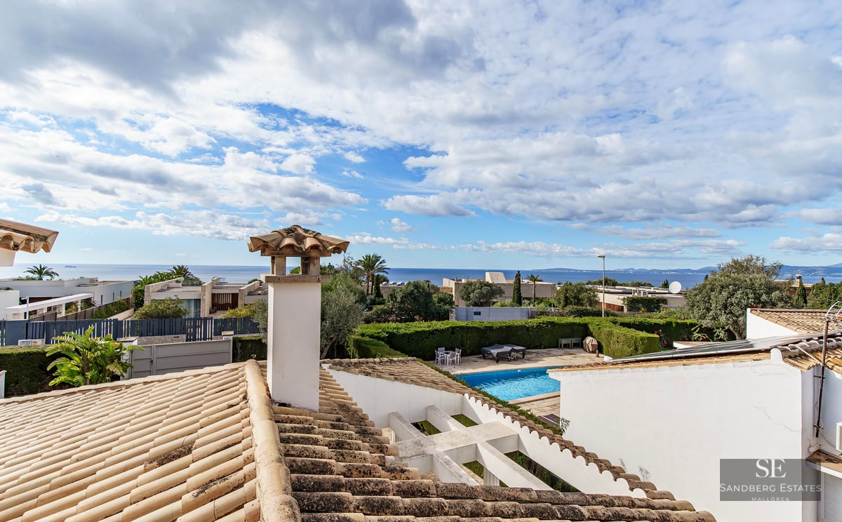 View from a tiled rooftop looking over a garden pool toward the Mediterranean Sea under a cloudy sky.