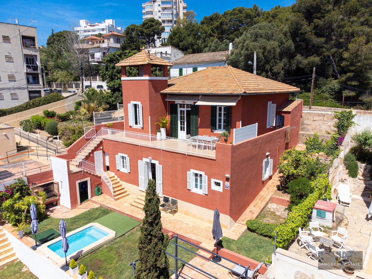 Aerial view of a terracotta-red villa with a private swimming pool, lush garden, and multiple sun terraces.