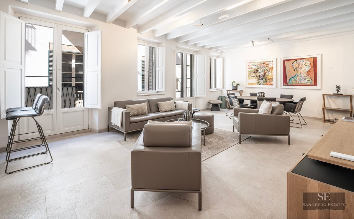 Spacious living room with taupe leather sofas, white beamed ceiling, and large windows with shutters.