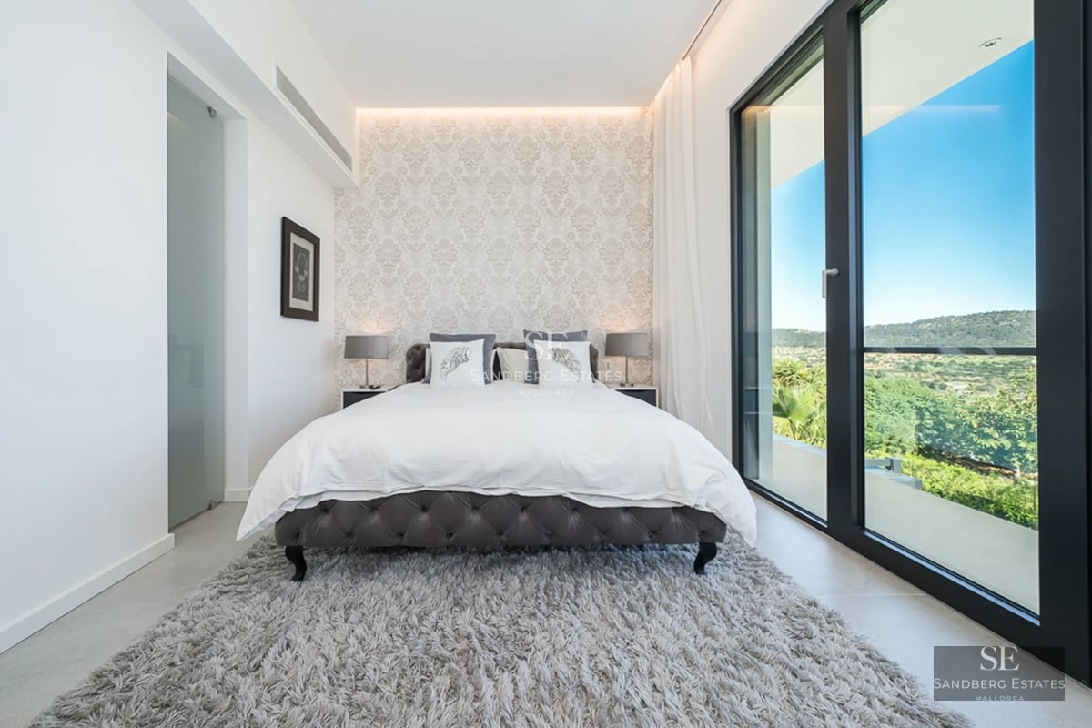 Spacious living room with large windows, light wood floors, natural lighting, and minimalist decor. View of a lush garden.