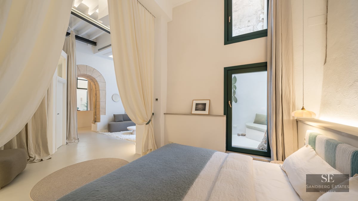Luxury bedroom with bed, cream curtains, a stone arch, and a view of a private patio.