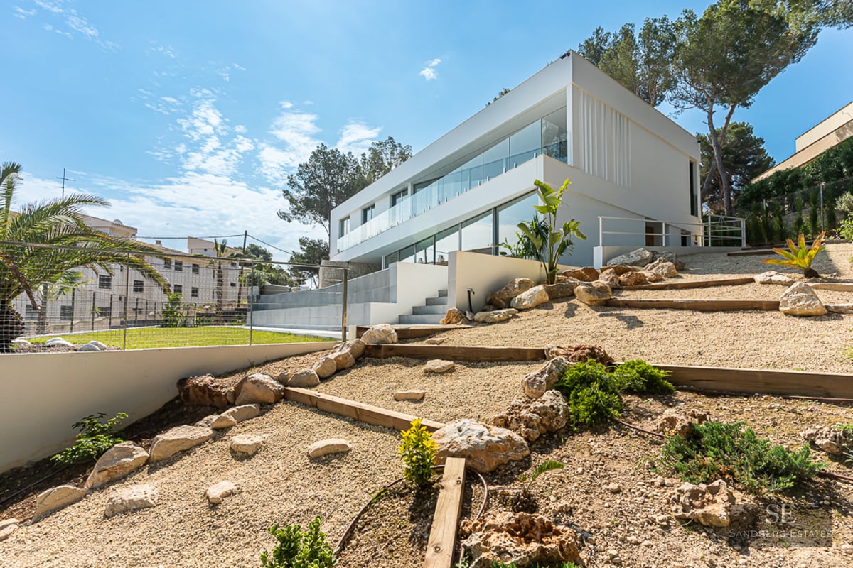 Side view of a modern two-story white villa with large glass windows and a tiered rock garden with gravel.