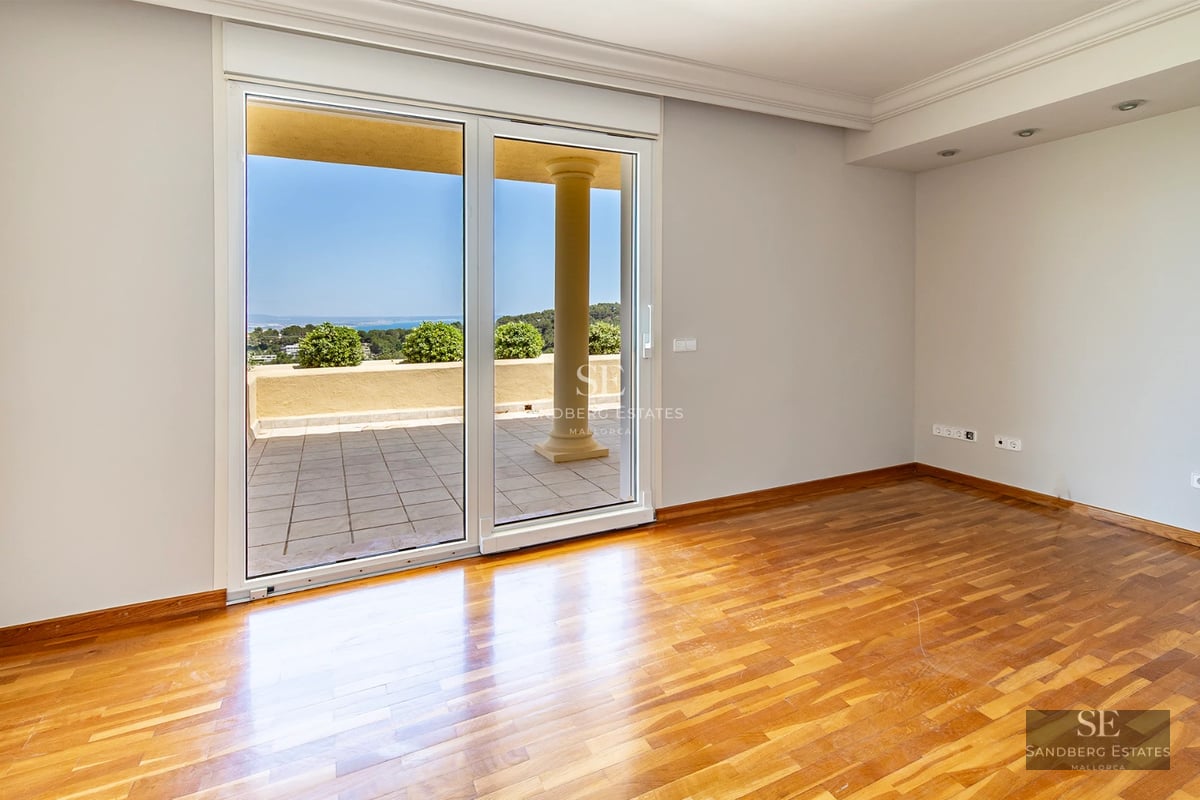 Spacious living room with floor-to-ceiling windows, light wood floors, white walls, and modern design furniture. Abundance of natural light.